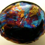 A lump of hafnium which has been oxidized on one side and exhibits thin film optical effects.